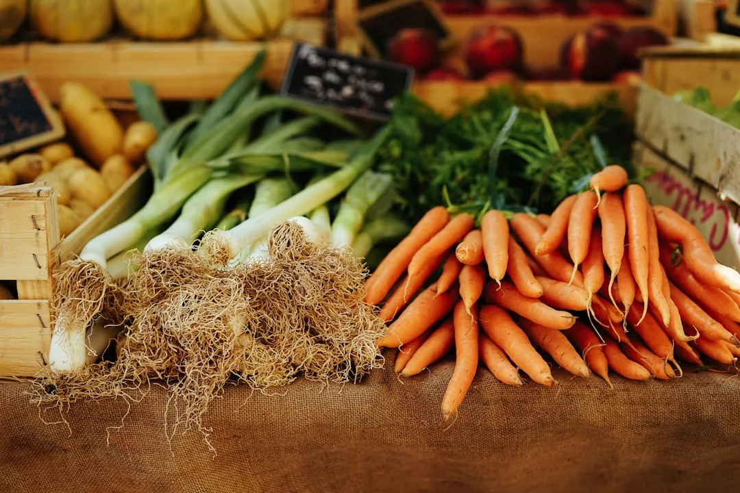 Un puesto del mercado de Mallorca muestra puerros frescos con raíces y un montón de zanahorias con hojas verdes, dispuestos uno junto al otro sobre una tela marrón, evocando el sencillo lujo de los productos locales.
