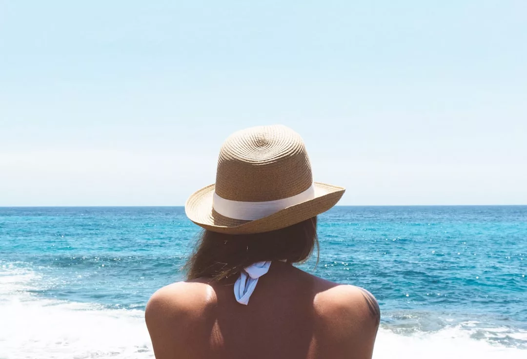 Una persona con sombrero de paja contempla el océano bajo un cielo despejado, captando el relajado lujo de las hermosas aguas azules de Mallorca.