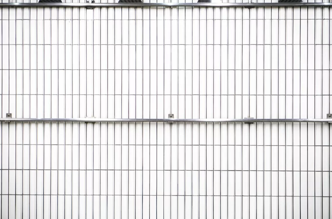 Pared de azulejos blancos con líneas de lechada negras verticales y horizontales, con dos barras metálicas horizontales: este elegante diseño aporta un toque de lujo inspirado en Mallorca a cualquier espacio moderno.