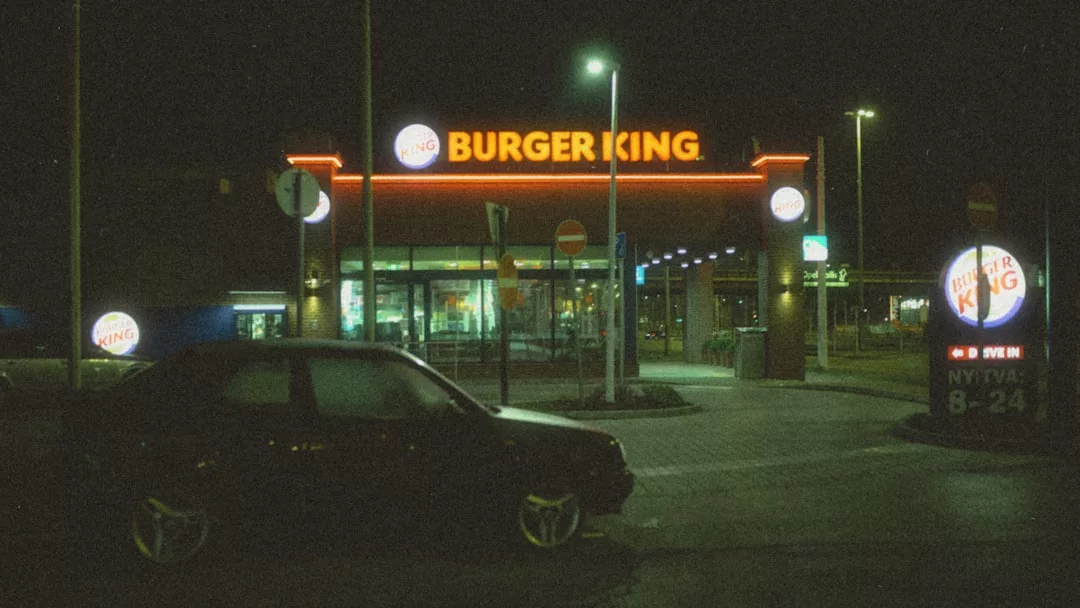 Un restaurante Burger King de noche en Mallorca con carteles luminosos, visto desde un aparcamiento donde un coche oscuro añade un toque de lujo a la escena.