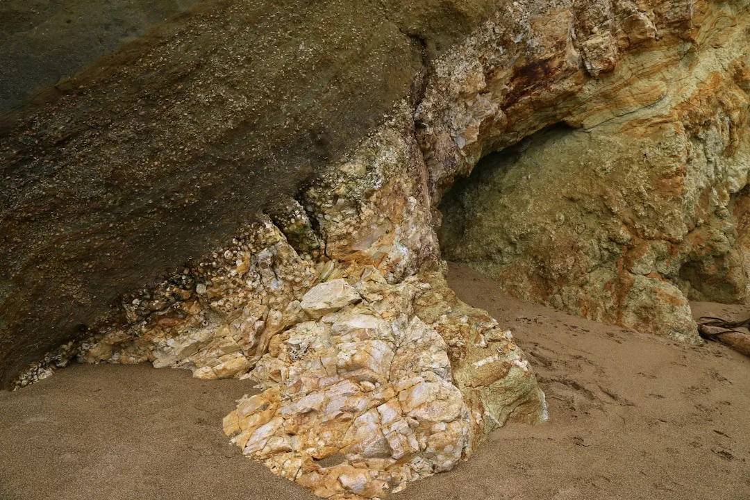 Primer plano de la entrada de una cueva rocosa en Mallorca, con formaciones de piedra con textura y suelo arenoso, que capta la esencia del lujo natural.