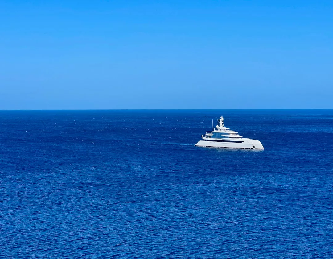 Un yate blanco navega por las tranquilas aguas del océano azul profundo bajo un cielo azul claro, capturando la esencia del lujo en la hermosa Mallorca.