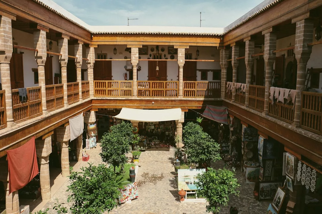 Patio al aire libre con exuberantes plantas, rodeado por dos niveles de balcones de madera, telas decoradas y una variedad de obras de arte y objetos expuestos en la planta baja: un toque de lujo mallorquín en cada detalle.