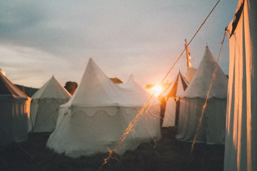 Las tiendas de lona blanca se instalan al aire libre al atardecer en Mallorca, con la luz del sol proyectando un cálido resplandor y las cuerdas visibles en primer plano, evocando una sensación de lujo y tranquilidad.