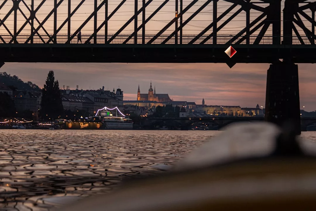 Vista de un paisaje urbano al atardecer a través de un puente sobre un río en Mallorca, con barcos iluminados y edificios de lujo brillando al fondo.