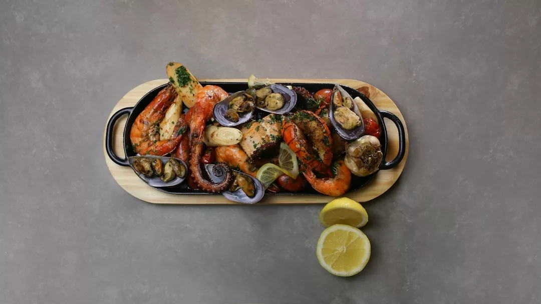 Un plato de marisco cocido, incluyendo gambas, almejas y pescado, se sirve en una tabla de madera con dos mitades de limón en el lado - trayendo un sabor de Mallorca lujo a su mesa.