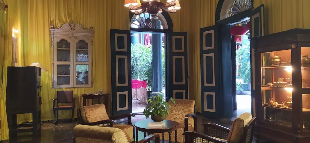Un salón de estilo vintage en Mallorca con cortinas amarillas, muebles de madera, una maceta sobre la mesa, vitrina, puertas altas y luz natural que añade un toque de lujo a través de la puerta abierta.