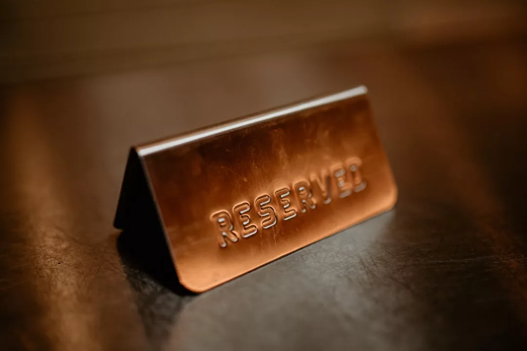 Un cartel de mesa metálico con la palabra "RESERVADO" en relieve, colocado sobre una superficie oscura, añade un toque de lujo que recuerda a las experiencias gastronómicas de lujo de Mallorca.