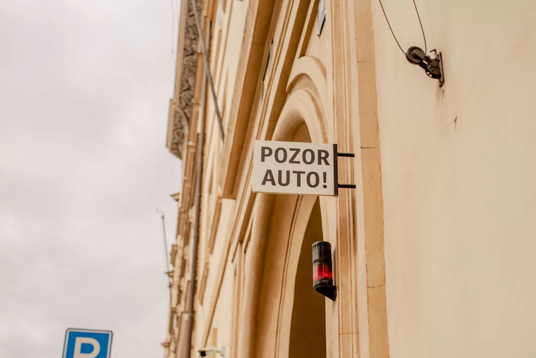 Un cartel que dice "POZOR AUTO!" está montado en la pared exterior de un edificio beige en Mallorca, con parte de una señal de aparcamiento azul visible en la esquina inferior izquierda, añadiendo un toque de Lujo urbano a la escena.