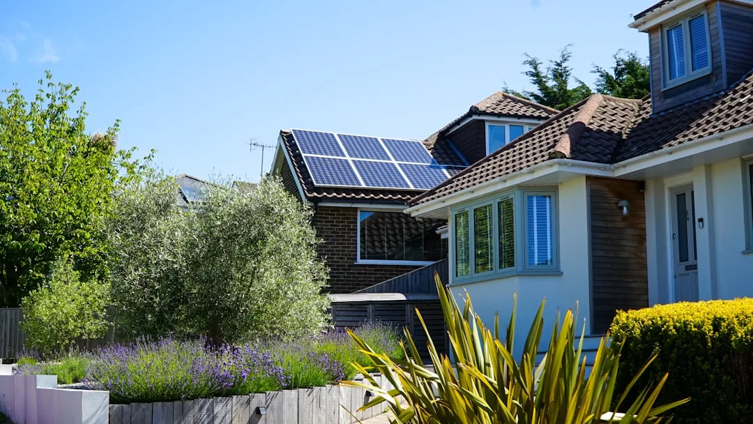 Una casa con paneles solares en el tejado rezuma lujo, rodeada de un exuberante jardín de plantas y arbustos verdes bajo el cielo azul despejado de Mallorca.