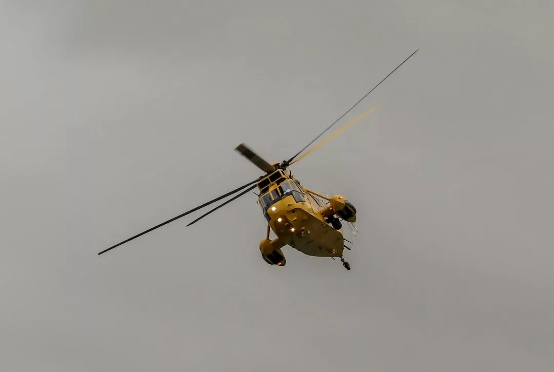 Un helicóptero amarillo, símbolo del lujo, vuela contra un cielo gris y nublado sobre Mallorca, vista desde abajo.
